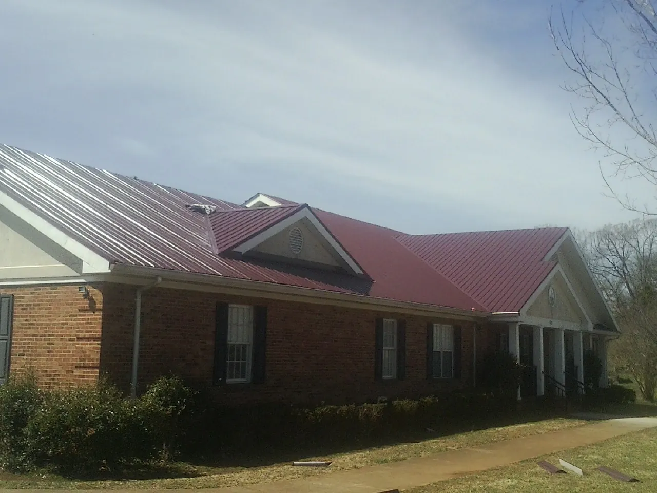 Red metal roof with gabled entries on a long brick building, from a Hail Damage Roof Repair job in Elizabethville