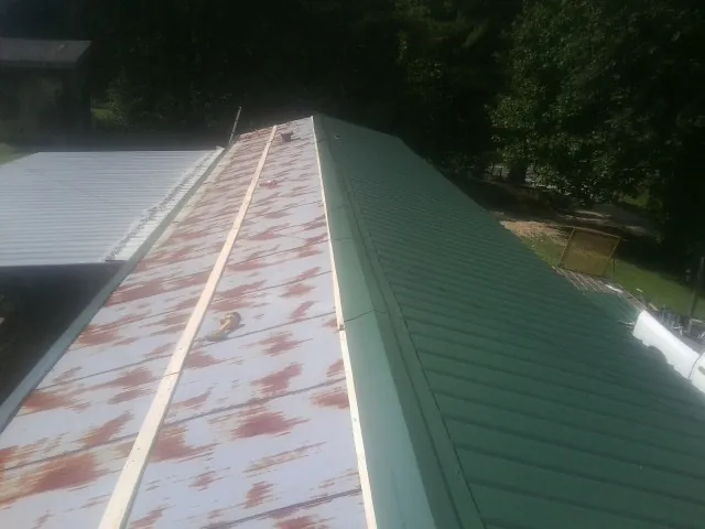 Old rusted panels beside newly installed green metal roofing in Elizabethville