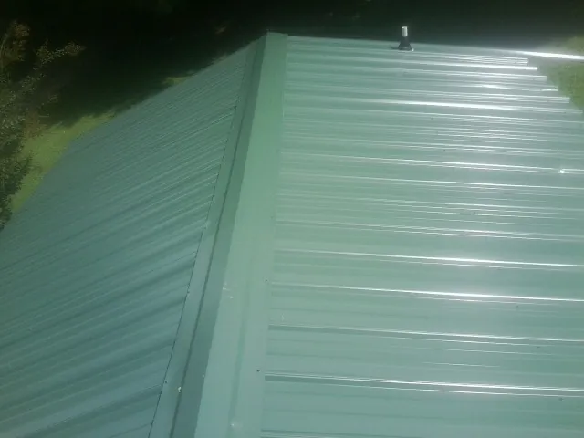 New green metal panels meeting at the ridge of a roof — Flat Roof Repair work by our crew in Elizabethville