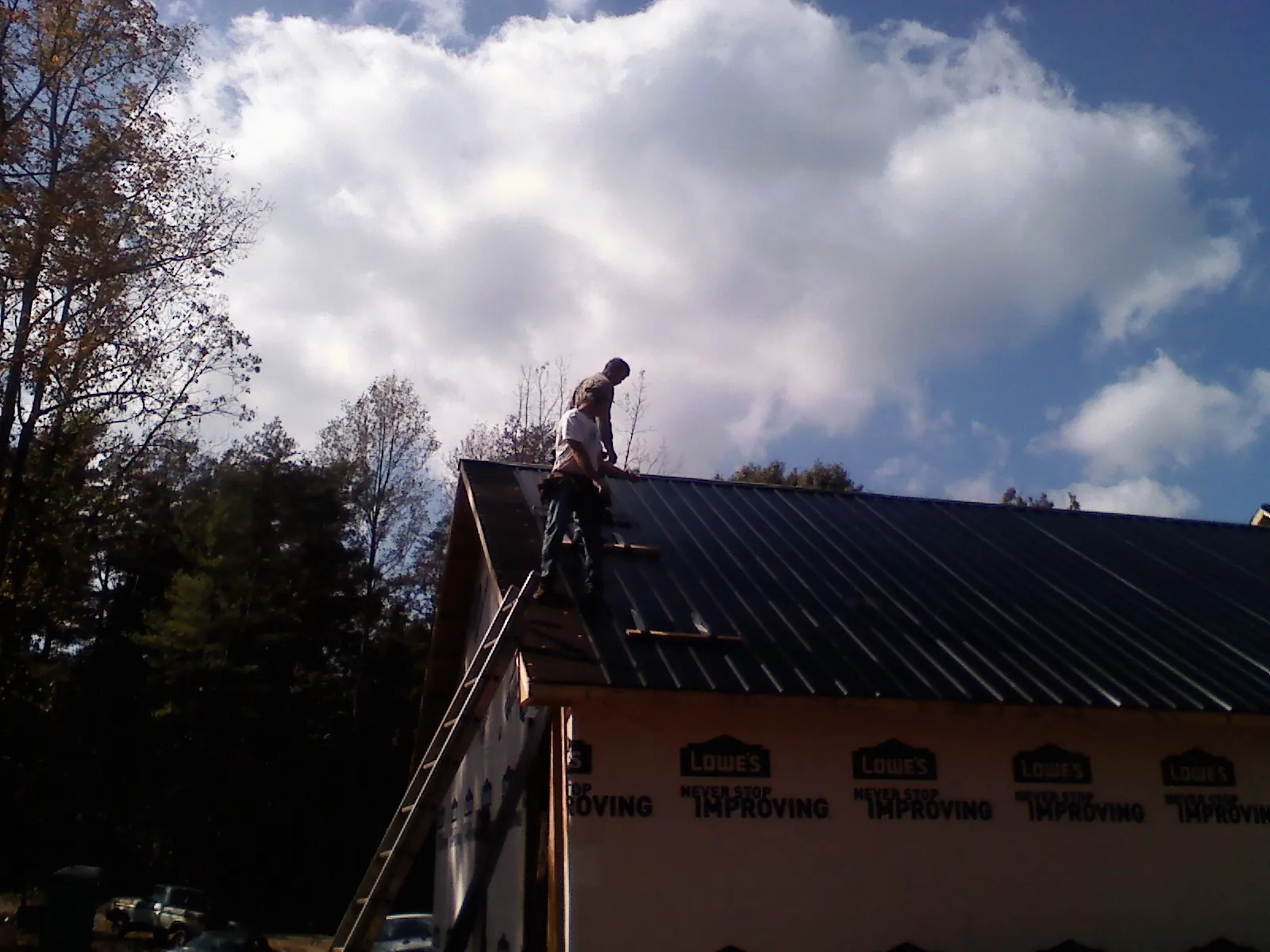 Roofer fastening dark metal panels high against a cloudy sky, from a Roof Inspection job in Elizabethville
