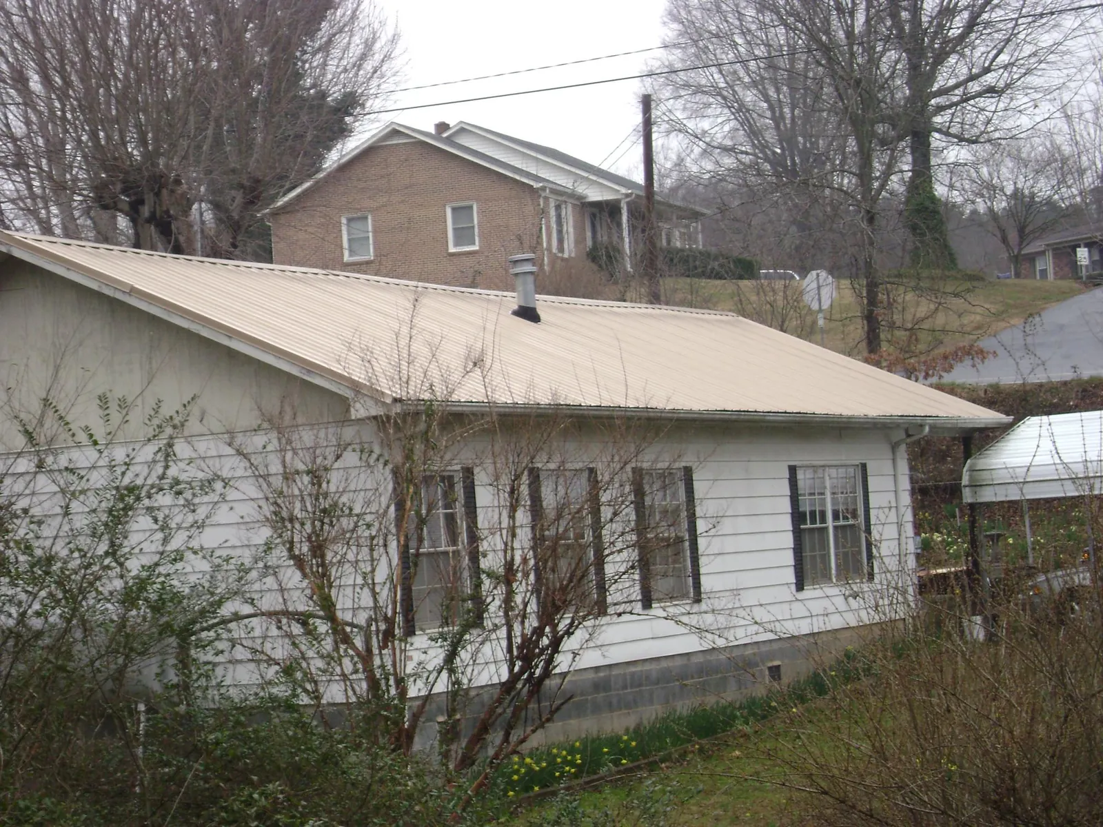 Tan metal roof on a white sided house set into a hillside — Commercial Roofing by Roofing Brothers in Elizabethville